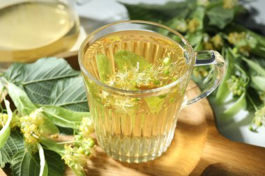 Fincanda lezzetli ıhlamur çayı, ışık masasında yapraklar ve çiçekler, yakın plan.