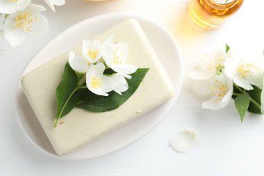 Sabun çubuğu, temel yağ ve yasemin çiçekleri beyaz ahşap masada, düz yatıyordu.