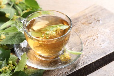 Fincanda lezzetli ıhlamur çayı, masada yapraklar ve çiçekler, yakın plan.