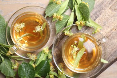 Fincanlarda nefis ıhlamur çayı, ahşap masada yapraklar ve çiçekler.