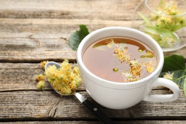 Lezzetli ıhlamur çayı, kaşık, yapraklar ve çiçekler ahşap masada, yakın plan.