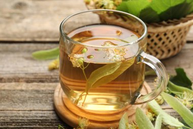 Fincanda lezzetli ıhlamur çayı, ahşap masada yapraklar ve çiçekler, yakın plan.