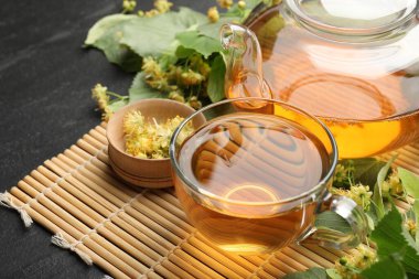 Fincanda lezzetli ıhlamur çayı, çaydanlık, koyu dokulu masa üzerinde yapraklar ve çiçekler, yakın plan.