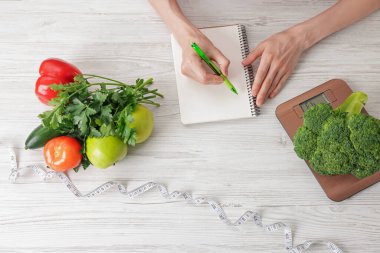 Hafif ahşap masada sağlıklı yiyecekler ve mezura ile beslenme planı geliştiren bir kadın.