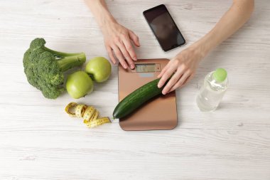 Mutfak terazisinde salatalık ağırlığında bir kadın açık ahşap masada, üst tarafta.