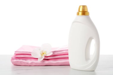 Bir şişe yumuşatıcı, üst üste yığılmış giysiler ve çiçek beyaz arka plana karşı mermer masa