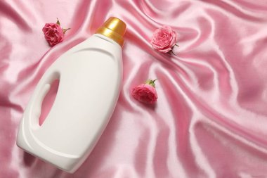 Bir şişe yumuşatıcı ve pembe kumaş üzerinde çiçekler, düz yatak. Metin için boşluk