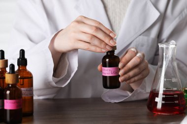 Laboratuardaki ahşap masada lüks parfüm üreten profesyonel parfümcü.