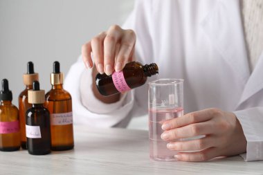 Laboratuvarda beyaz ahşap masada lüks parfüm üreten profesyonel bir parfümcü.