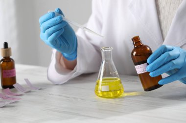 Laboratuvarda beyaz ahşap masada lüks parfüm üreten profesyonel bir parfümcü.