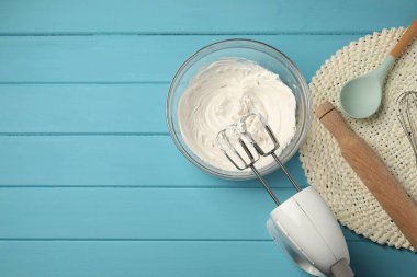El çırpıcı, krem şanti kasede, merdane ve kaşık açık mavi ahşap masada, düz yerde. Metin için boşluk