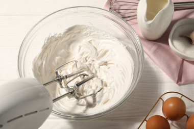 Beyaz ahşap masada çırpılmış krema, yumurta ve diğer ürünlerle karıştırıcı.