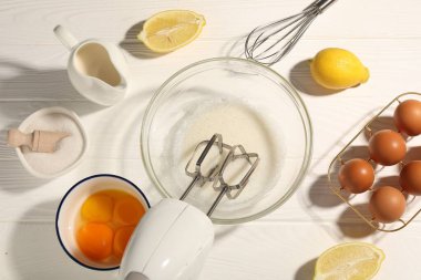 El çırpıcı, kasede yumurta beyazı, beyaz ahşap masa üzerinde yumurta ve diğer ürünler, düz konum