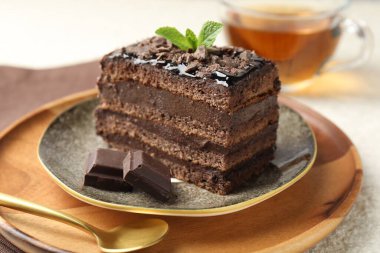 Bir parça nefis çikolatalı kek, üzerinde nane ve çay, yakın plan.