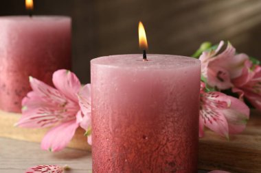 Beyaz ahşap masada yanan mumlar ve zambak çiçekleri, yakın plan.