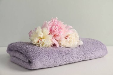 Açık gri arkaplanda yumuşak havlu ve şakayık çiçekleri, yakın plan.