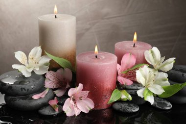 Yanan mumlar, kaplıca taşları ve ıslak siyah masada güzel çiçekler, yakın plan.