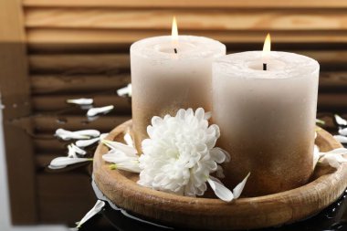 Islak siyah ayna yüzeyinde yanan mumlar ve güzel çiçekler, yakın plan.