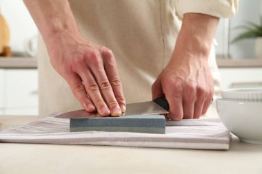 Kapalı alanda bej masa bileyicisiyle bıçak bileyen bir adam.