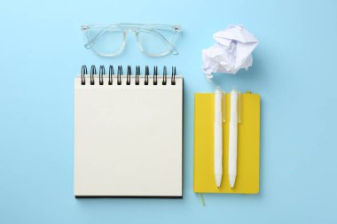 Defterler, gözlükler, buruşmuş kağıtlar ve kalemler açık mavi arka plan, düz uzanış