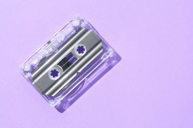 Menekşe arka planında manyetik bantlı bir ses kaseti, üst görüntü. Metin için boşluk