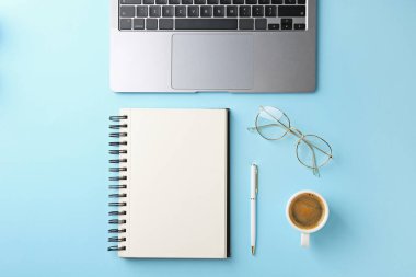 Not defteri, kalem, dizüstü bilgisayar, bardaklar ve kahve açık mavi arka planda, düz konum