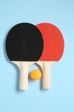 Masa tenisi raketleri ve top açık mavi arka planda, düz yatıyordu.