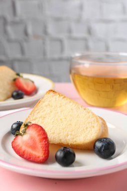 Bir parça meyveli kek ve pembe masada çay, yakın plan.