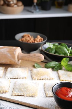 Pişmemiş ravioli, merdane, bolonez, sos ve fesleğen siyah masada, yakın plan.