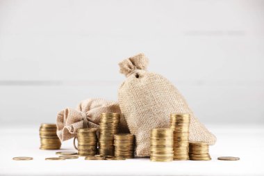 Çantalar ve istiflenmiş paralar beyaz masa üzerinde ışık arka planına karşı