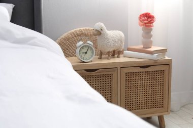 Yatağın yanında çalar saati, dekorasyonu ve kitapları olan bir komodin.