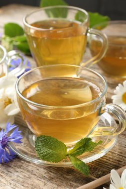 Cam bardaklarda aromatik bitki çayı, ahşap masada nane ve çiçekler, yakın plan.