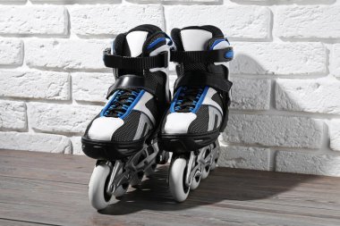 Beyaz tuğla duvarın yanındaki ahşap masada bir çift paten.