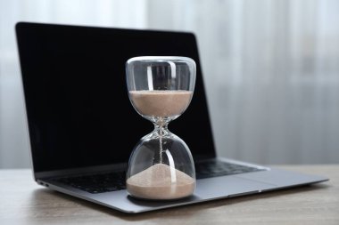 Son teslim tarihi. Kapalı alandaki ahşap masada akan kum ve dizüstü bilgisayarlı kum saati.