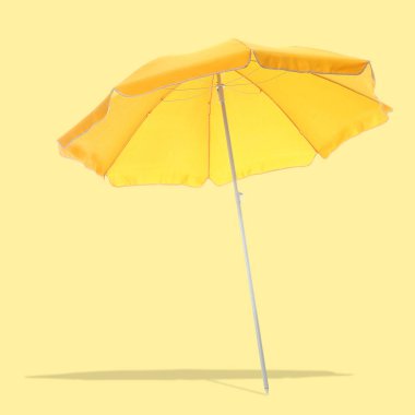Parlak kumsal şemsiyesi soluk sarı arka planda gölge bırakıyor