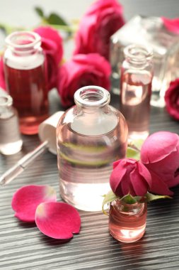 Aromatik esanslı parfüm şişelerini aç ve gri ahşap masada güller, yakın plan.