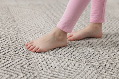 Evdeki gri halıda yürüyen kız, yakın plan.