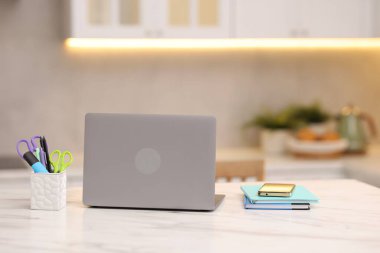 Laptop, akıllı telefon ve kırtasiye malzemeleri mutfaktaki beyaz mermer masada.
