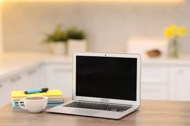 Boş ekranlı dizüstü bilgisayar, mutfaktaki ahşap masada bir fincan sıcak içecek ve kırtasiye malzemesi. Tasarım için model