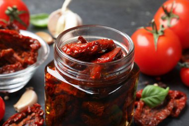 Lezzetli güneşte kurutulmuş domatesler ve taze sebzeler siyah masada, yakın plan.