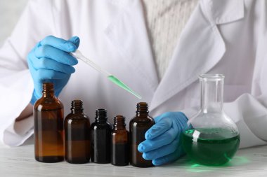 Laboratuvarda beyaz ahşap masada lüks parfüm üreten profesyonel bir parfümcü.