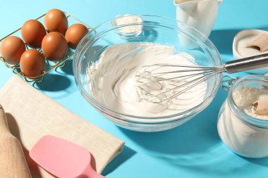 Açık mavi masada çırpılmış krema, yumurta ve diğer ürünlerle çırpın.
