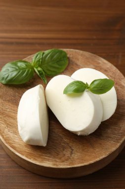 Nefis mozzarella peyniri parçaları ve fesleğen yaprakları ahşap masada, yakın plan.