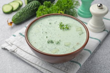 Lezzetli salatalık çorbası ve açık gri masadaki malzemeler, yakın plan.