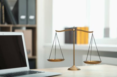 Ofisteki ahşap masada dizüstü bilgisayarı ve terazisi olan yargıcın iş yeri, yakın plan.