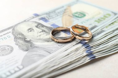 İki altın alyans ve bir dolarlık banknotlar beyaz masada, yakın plan.