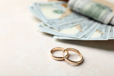 Beyaz masada iki altın alyans ve bir dolarlık banknotlar, yakın plan. Metin için boşluk