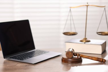 Yargıç. Dizüstü bilgisayar, tokmak, terazi ve ofisteki ahşap masa üzerine kitap, seçici odaklanma.