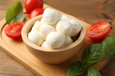 Lezzetli mozarella topları, domatesler ve fesleğenler ahşap masada, yakın plan.