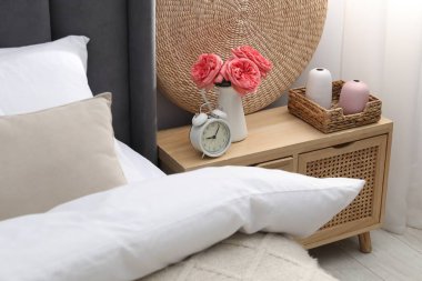 Yatağın yanında alarm saati ve dekorasyonu olan komodinin yanında.